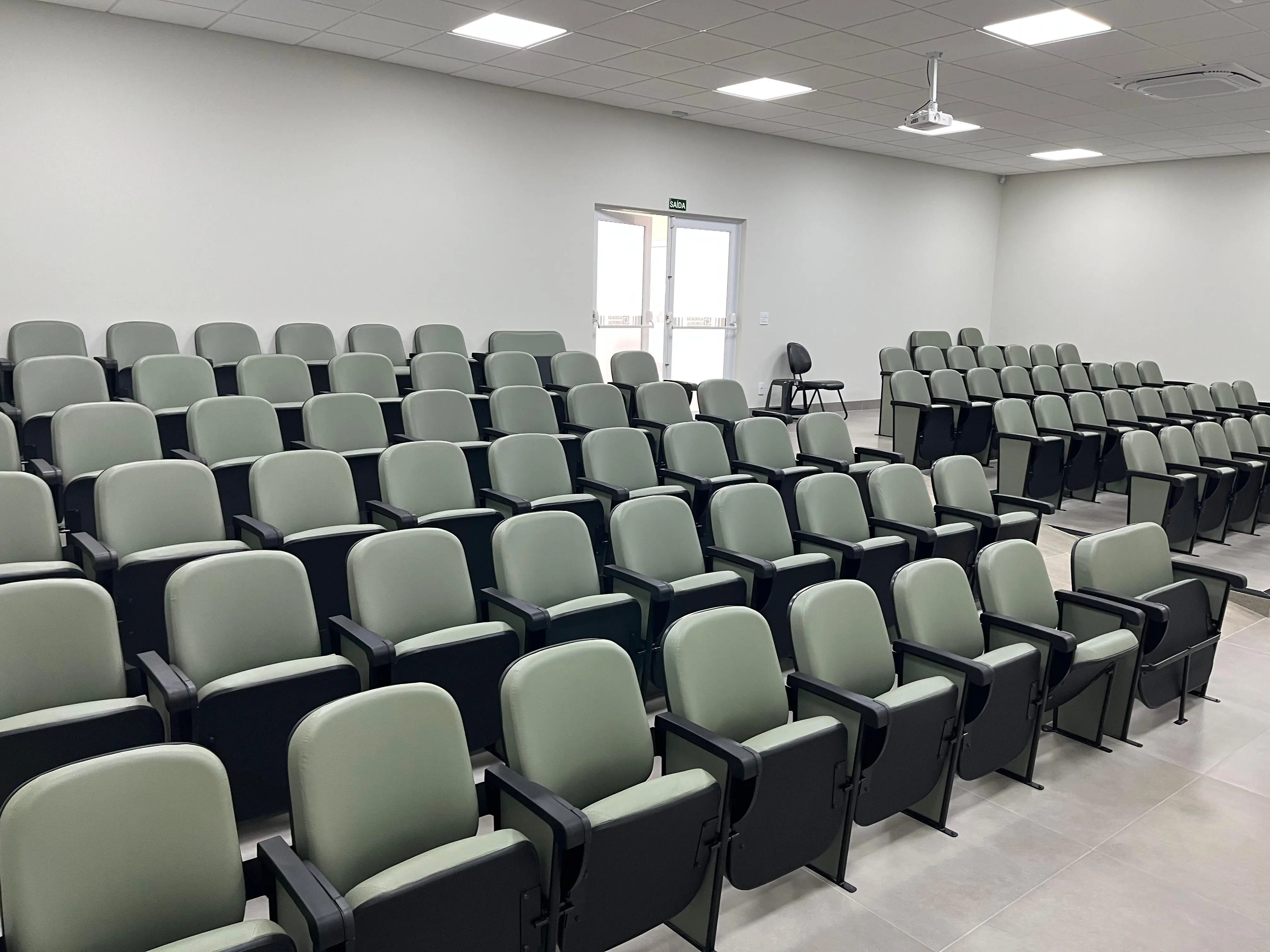 Na foto mostra as cadeiras do auditório numa visão de lado onde mostra a porta de entrada e saída do auditório.